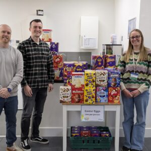 Three people with a mound of chocolate Easter eggs donated to Exeter Foodbank